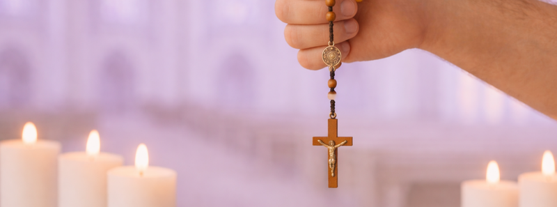 Hand holding a rosary with lit candles in the background1
